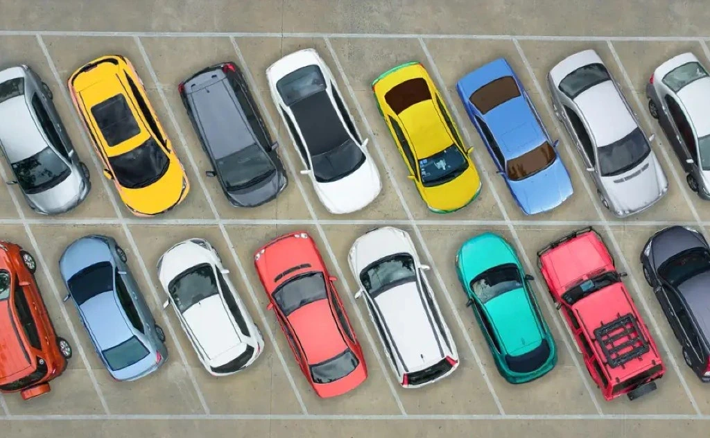 Vue aérienne d'un parking : deux rangées de berlines, citadines y SUV colorés sur emplacements marqués de lignes blanches — flota d'empresa