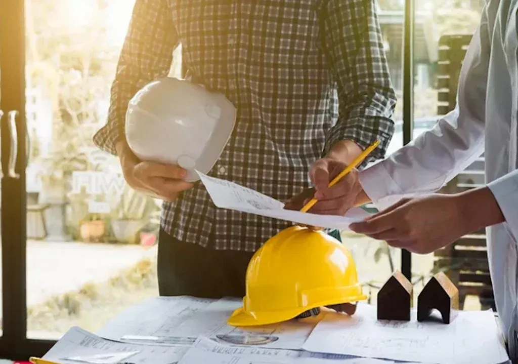 Profesionales du construcción étudiant de los plans sur una table, casques de obra y maquettes — seguro construction y travaux publics RMA Tánger