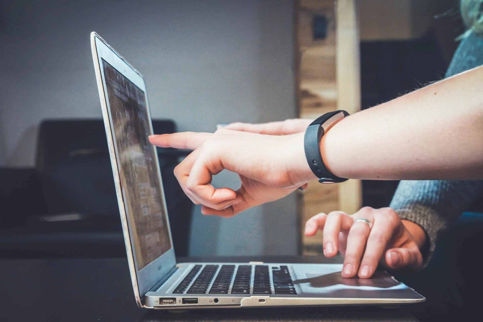 Gros plan sur deux mains près d'un ordinateur portable : una personne pointe l'écran, l'autre utilise le pavé tactile — collaboration y soutien profesional