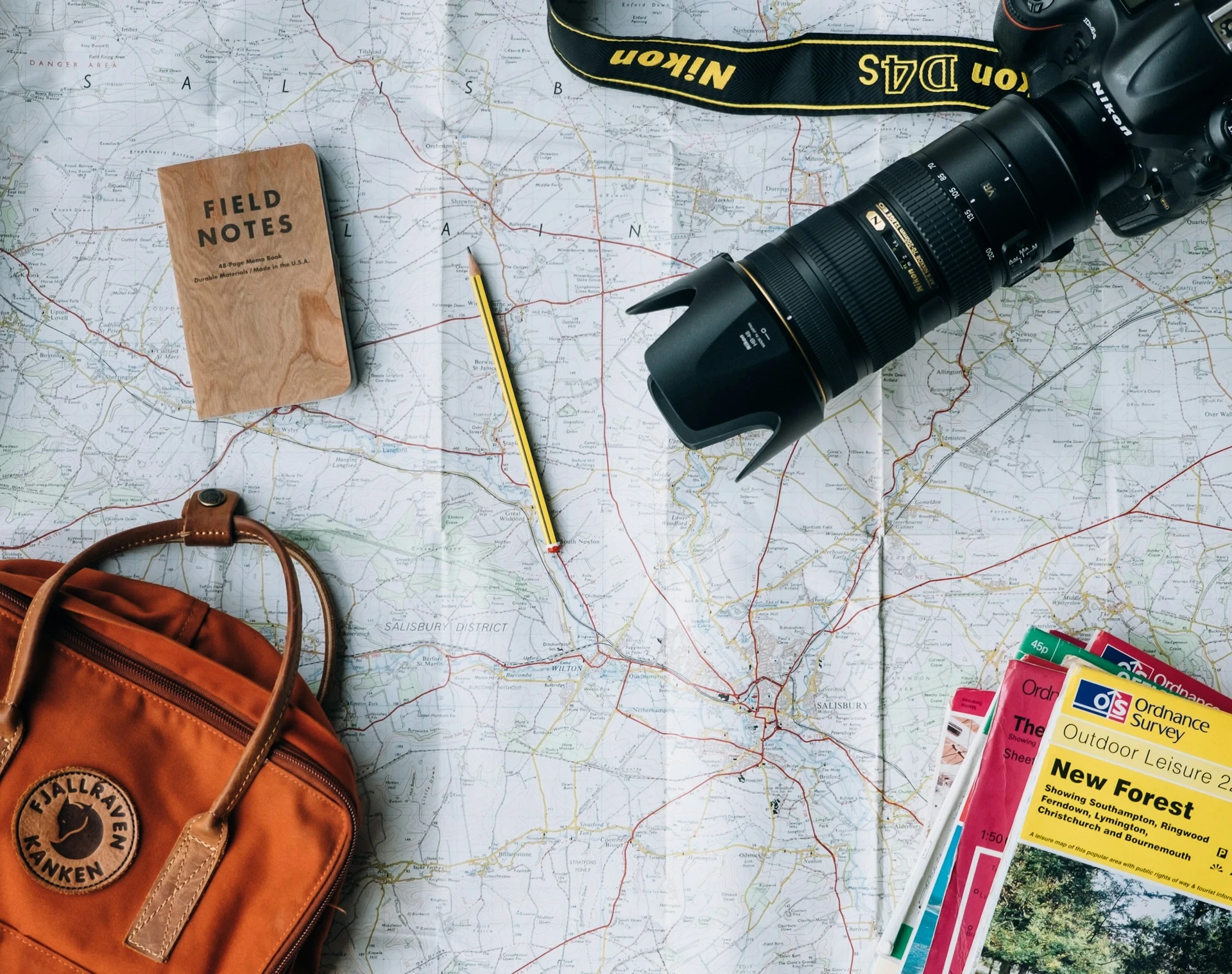 Vue du dessus : mapa topographique dépliée, petit carnet, appareil photo reflex y guides outdoor — mobilité internationale y cobertura salud à l'étranger